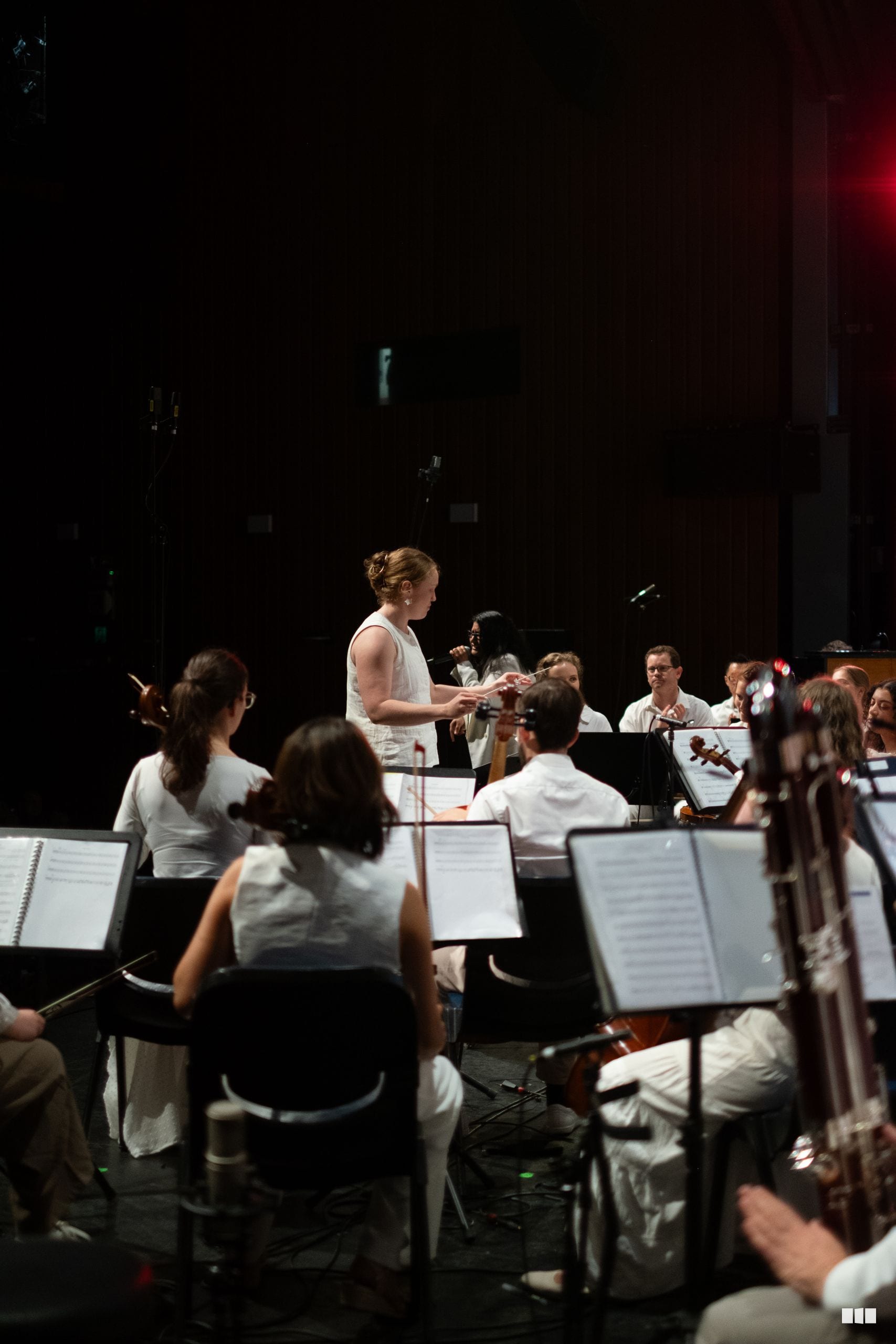 A conductor leads a string section during an orchestral rehearsal or performance on stage.