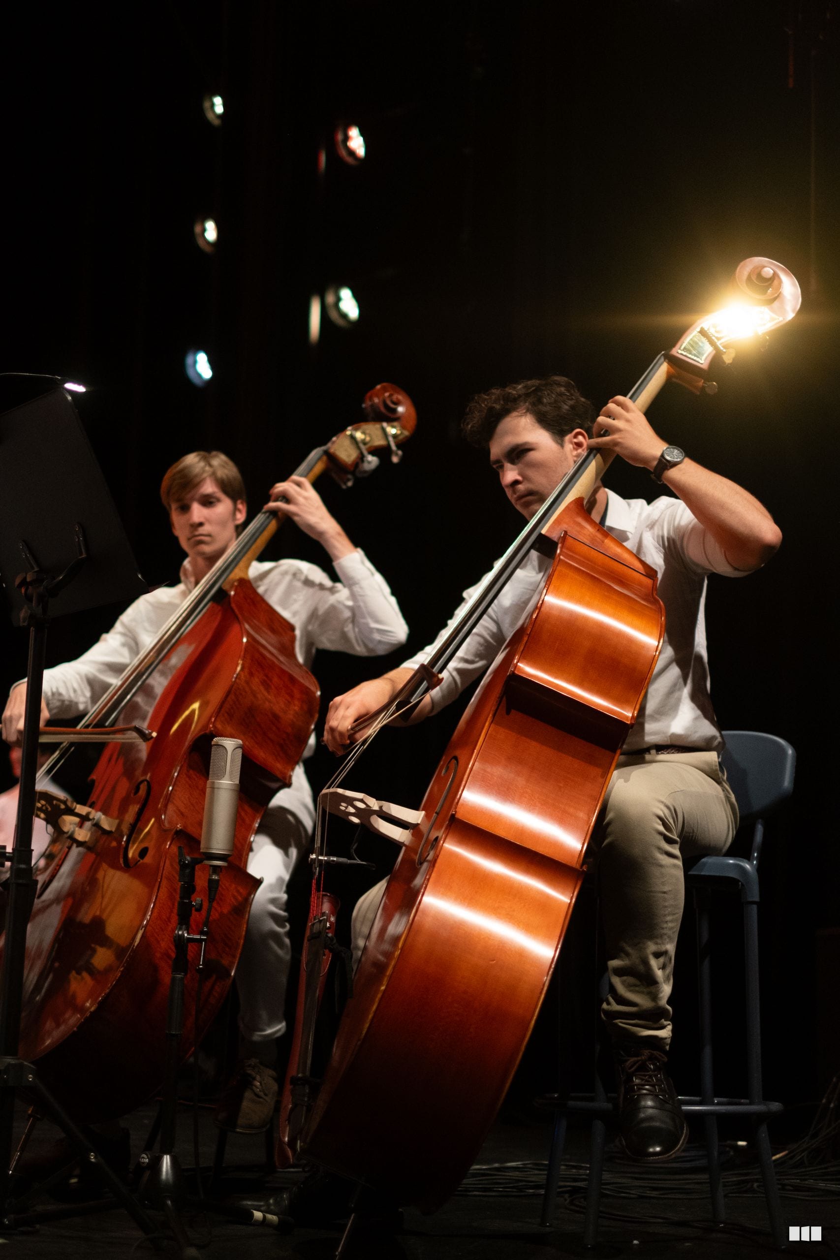 Two cellists perform together on stage under theatrical lighting during an orchestral concert.