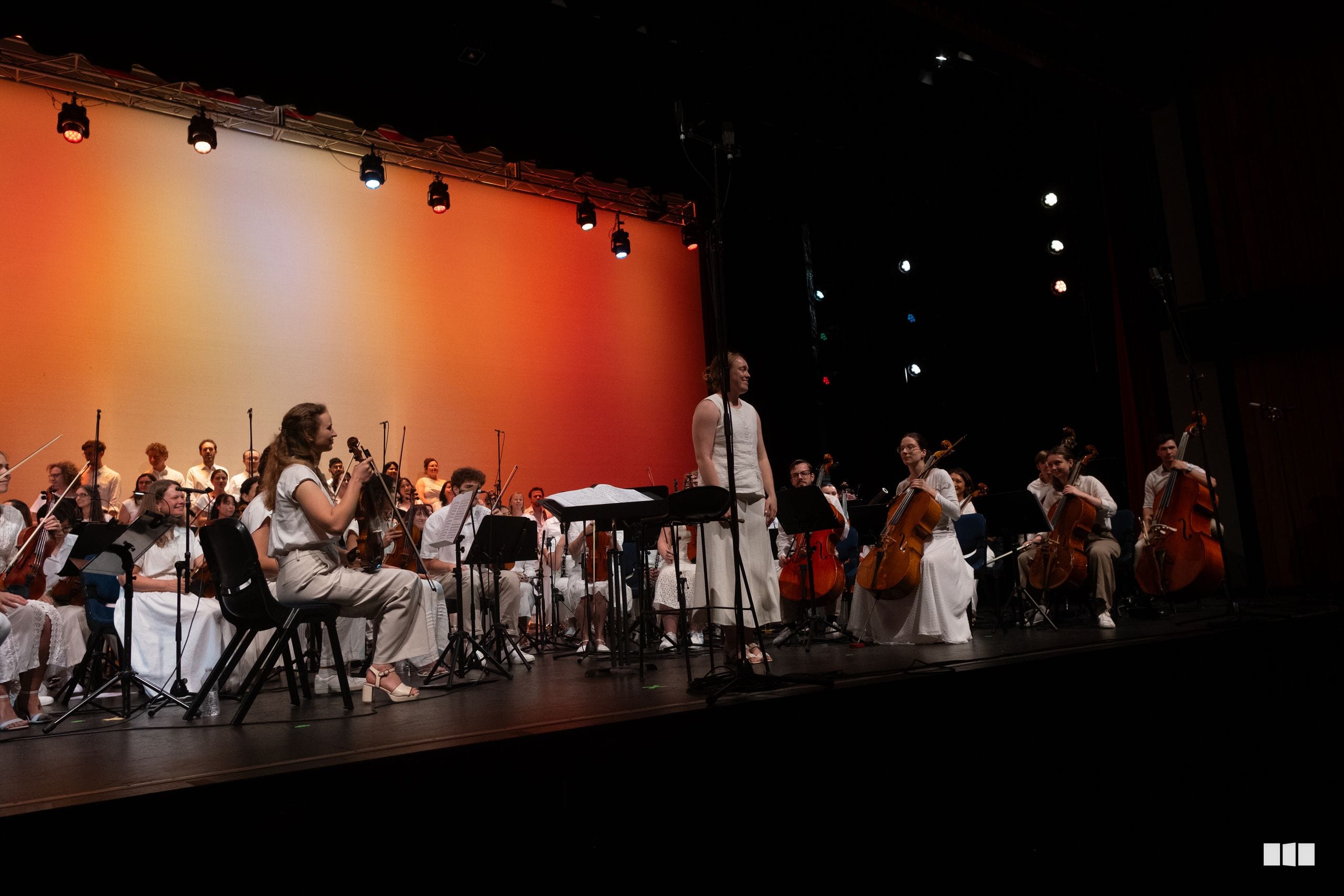 A soprano soloist performs with the orchestra on stage, accompanied by string and wind sections under warm stage lighting.