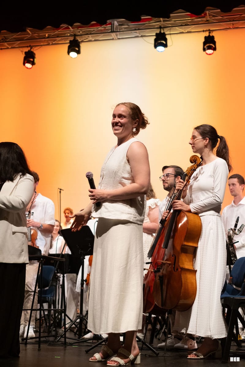 A conductor addresses the orchestra and choir members on stage during a performance.