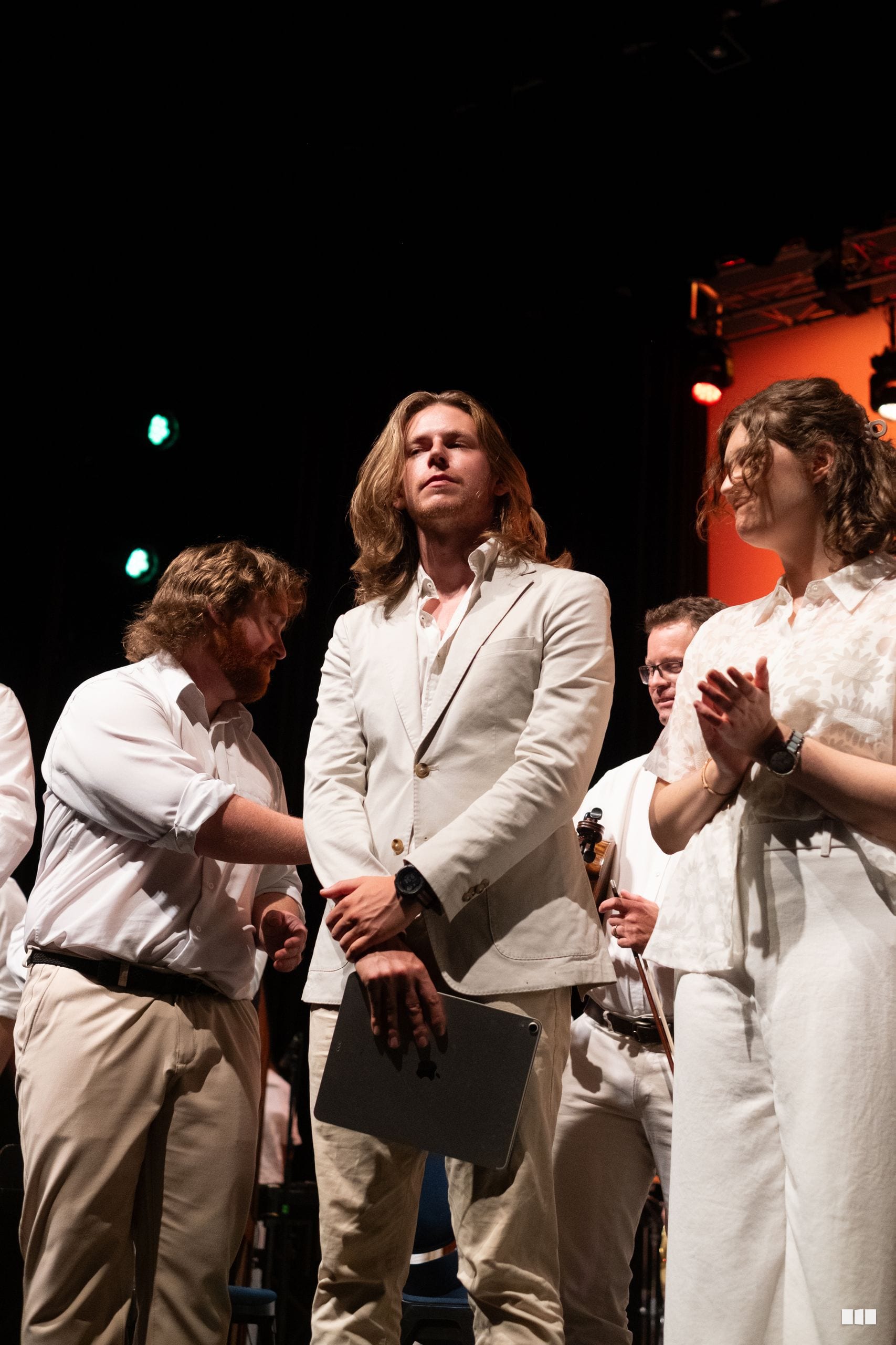 Several performers in cream and white formal attire stand together on stage during what appears to be a presentation or performance moment.