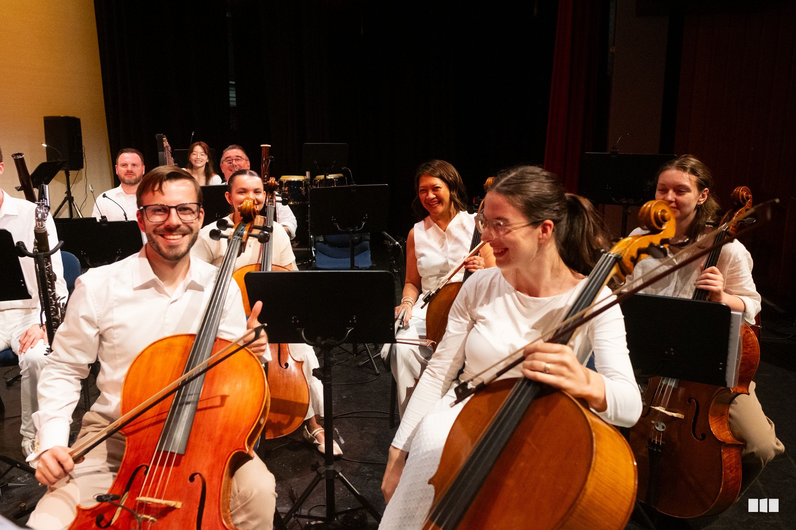 String section musicians in white attire performing together during an orchestral rehearsal or concert.