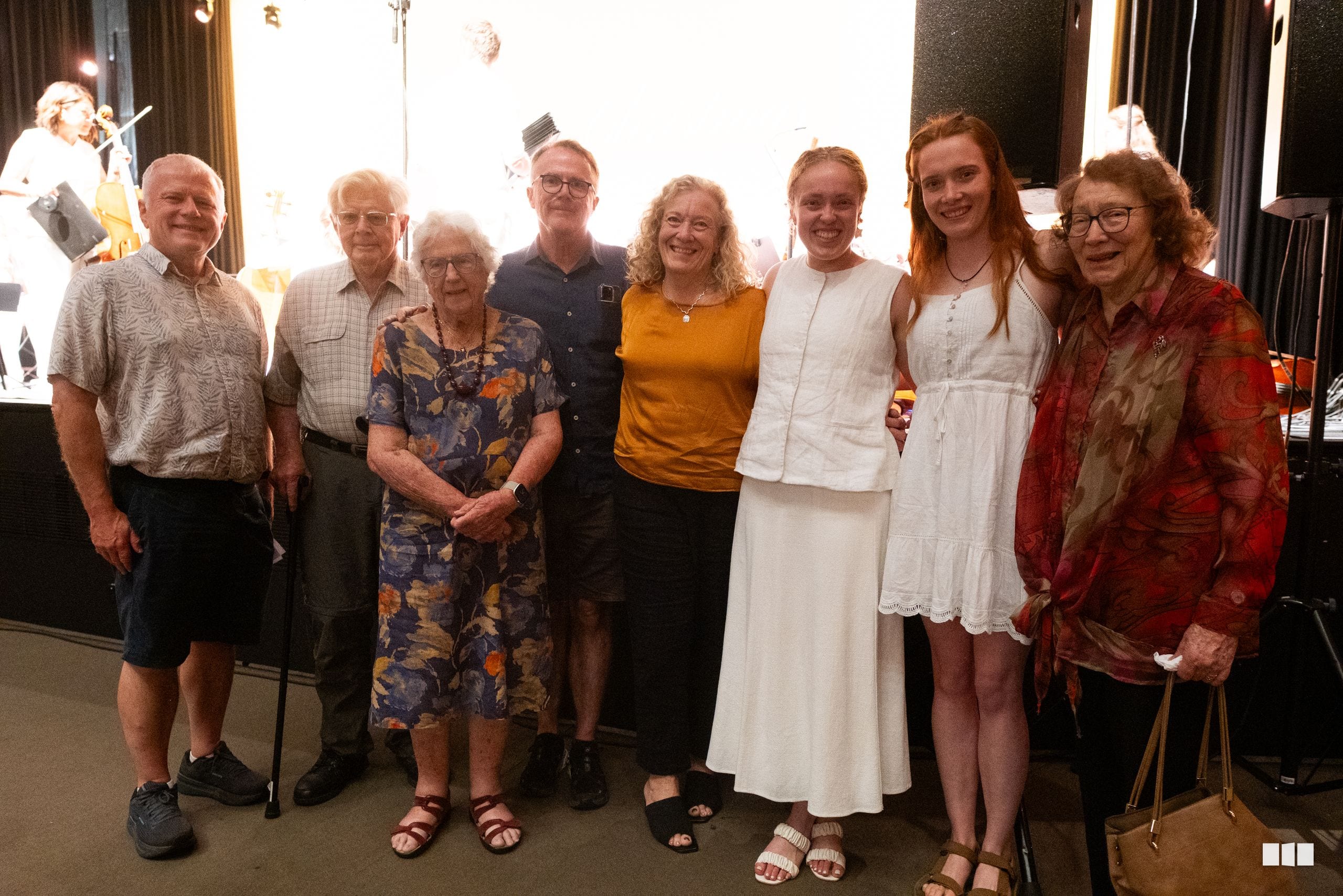 A group of orchestra and choir members pose together for a photo in front of stage lighting.