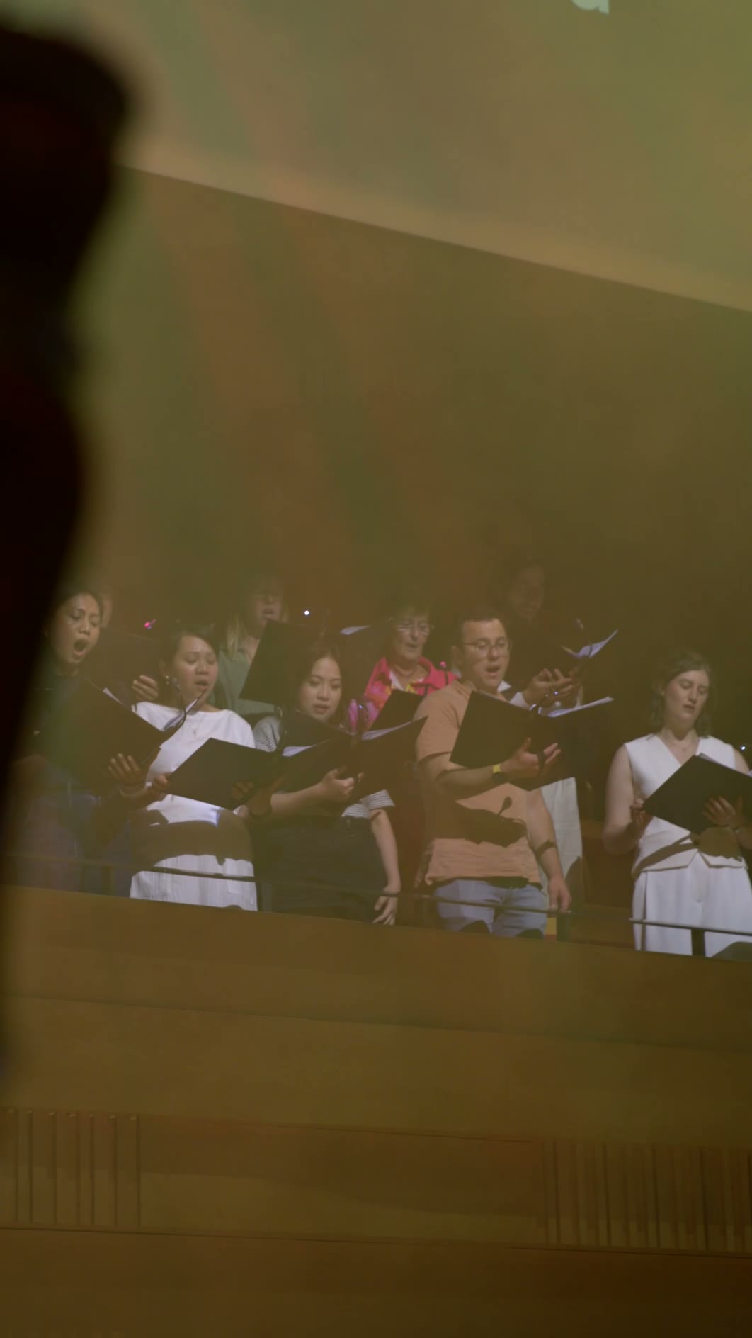A choir performs during a service, with singers holding hymnals and wearing formal robes with white stoles.