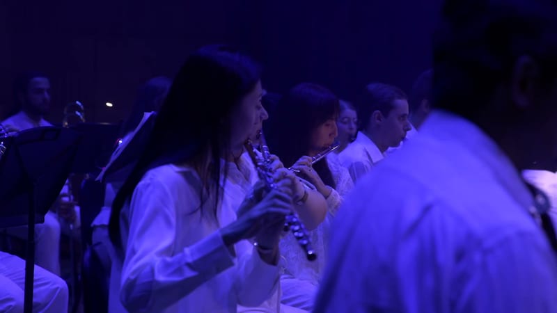 Woodwind musicians perform together during an orchestral concert under blue stage lighting.