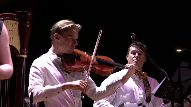 Two violinists perform together on stage during an orchestral concert.