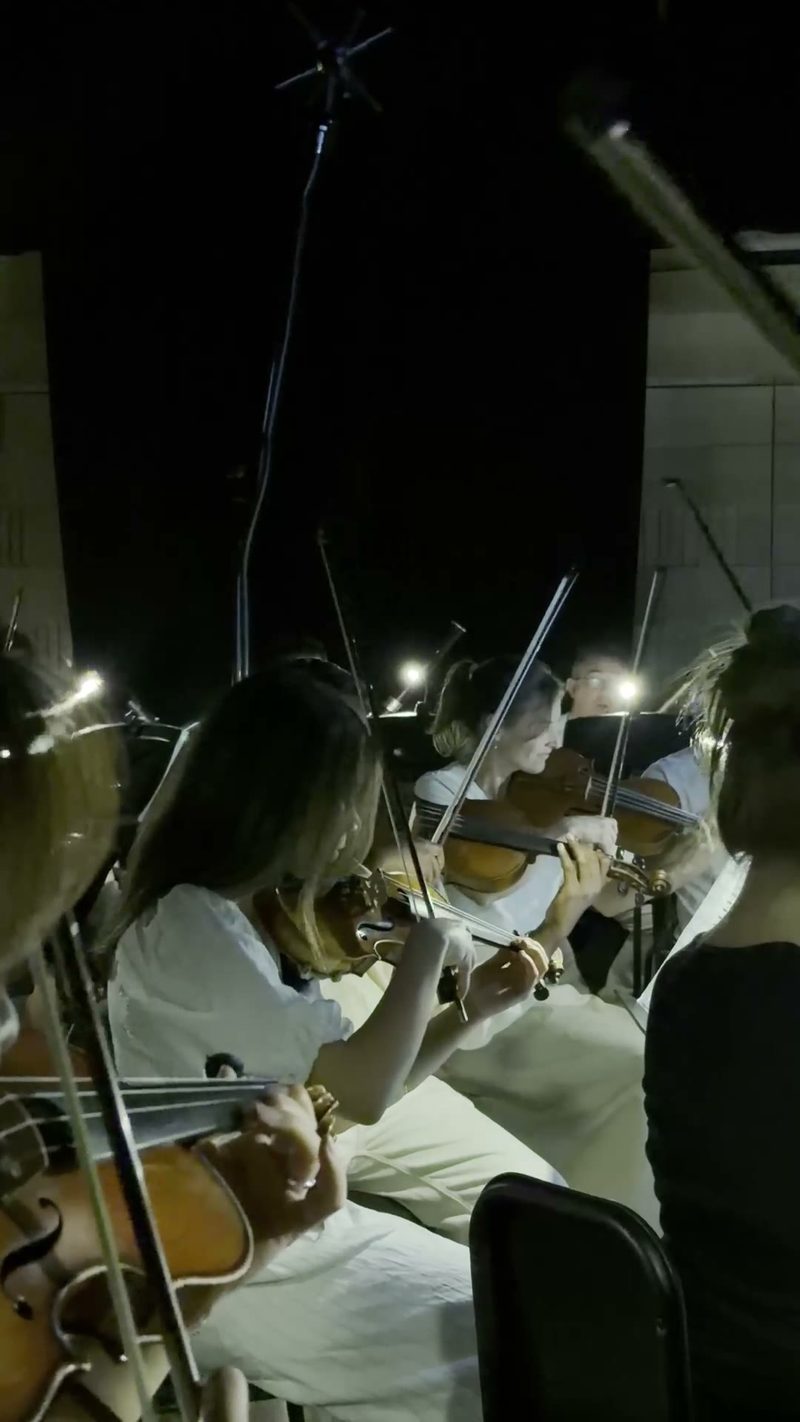 String players perform together during an evening rehearsal or concert under stage lighting.
