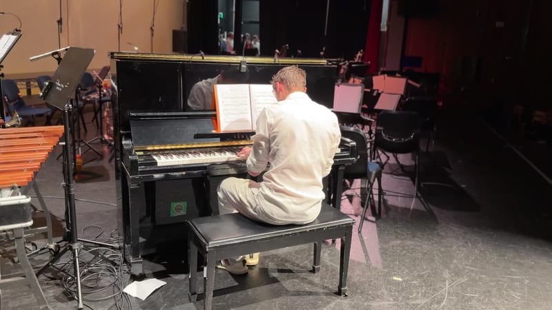 A pianist performs at the grand piano during a rehearsal or recording session on stage.