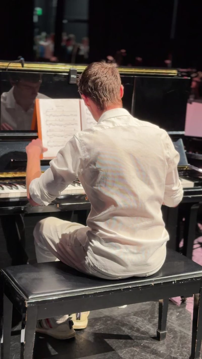 A pianist in a white shirt performs at a grand piano during an orchestral concert.