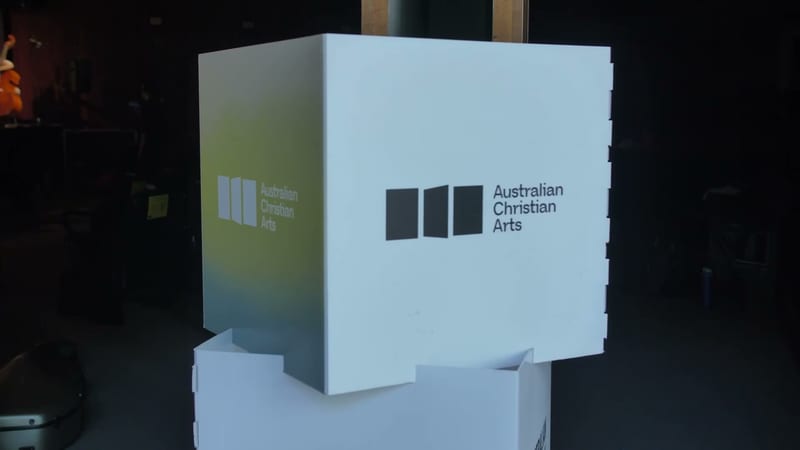 A illuminated display cube showing the Australian Christian Arts logo with three vertical rectangular shapes and text.
