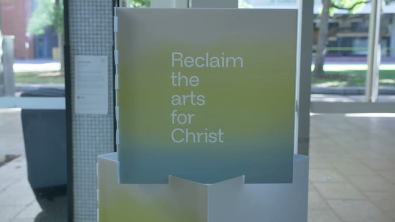 A frosted glass panel displays the message 'Reclaim the arts for Christ' at an outdoor venue entrance.