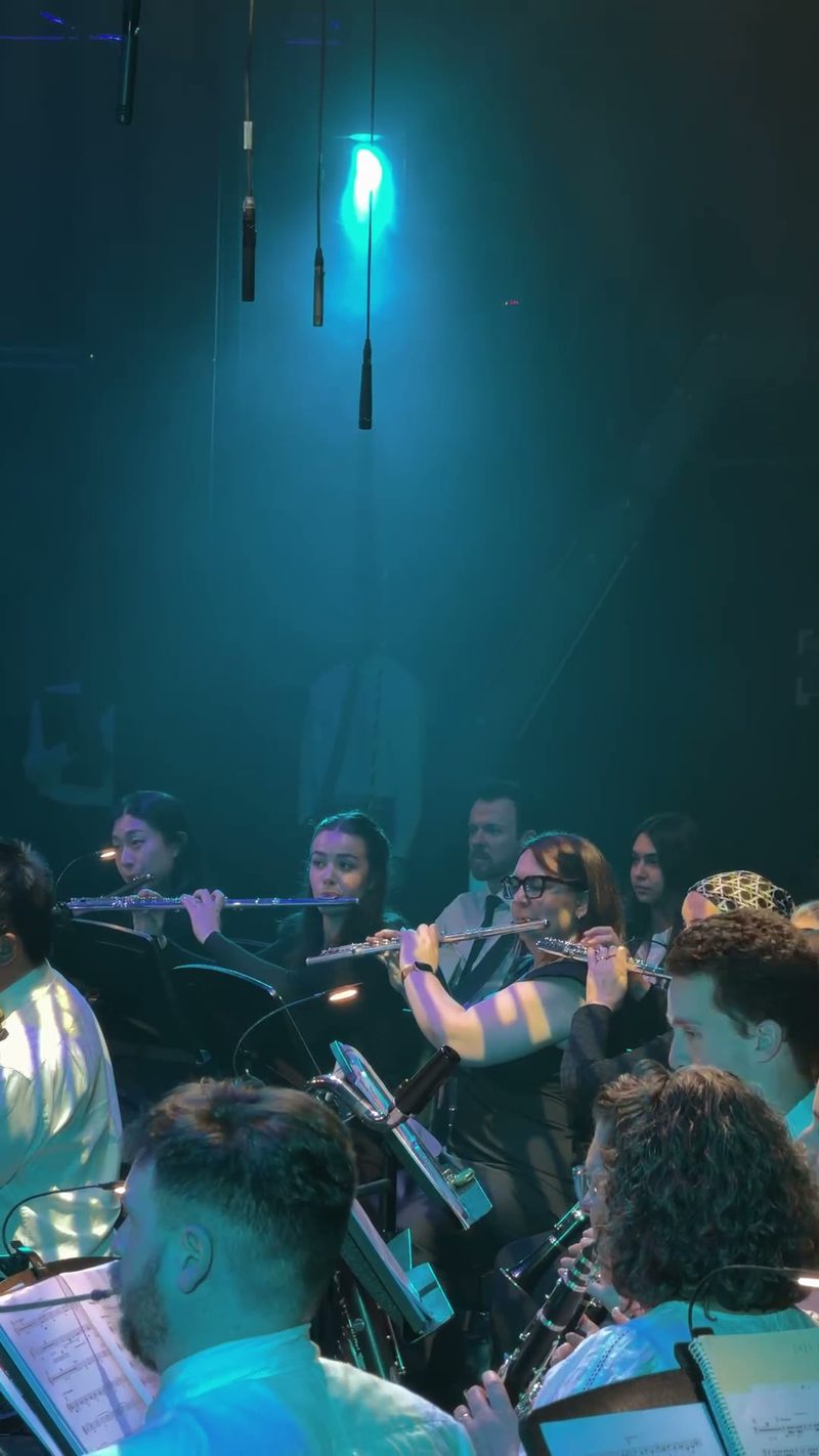 A group of musicians performing with flutes in a symphony orchestra setting.