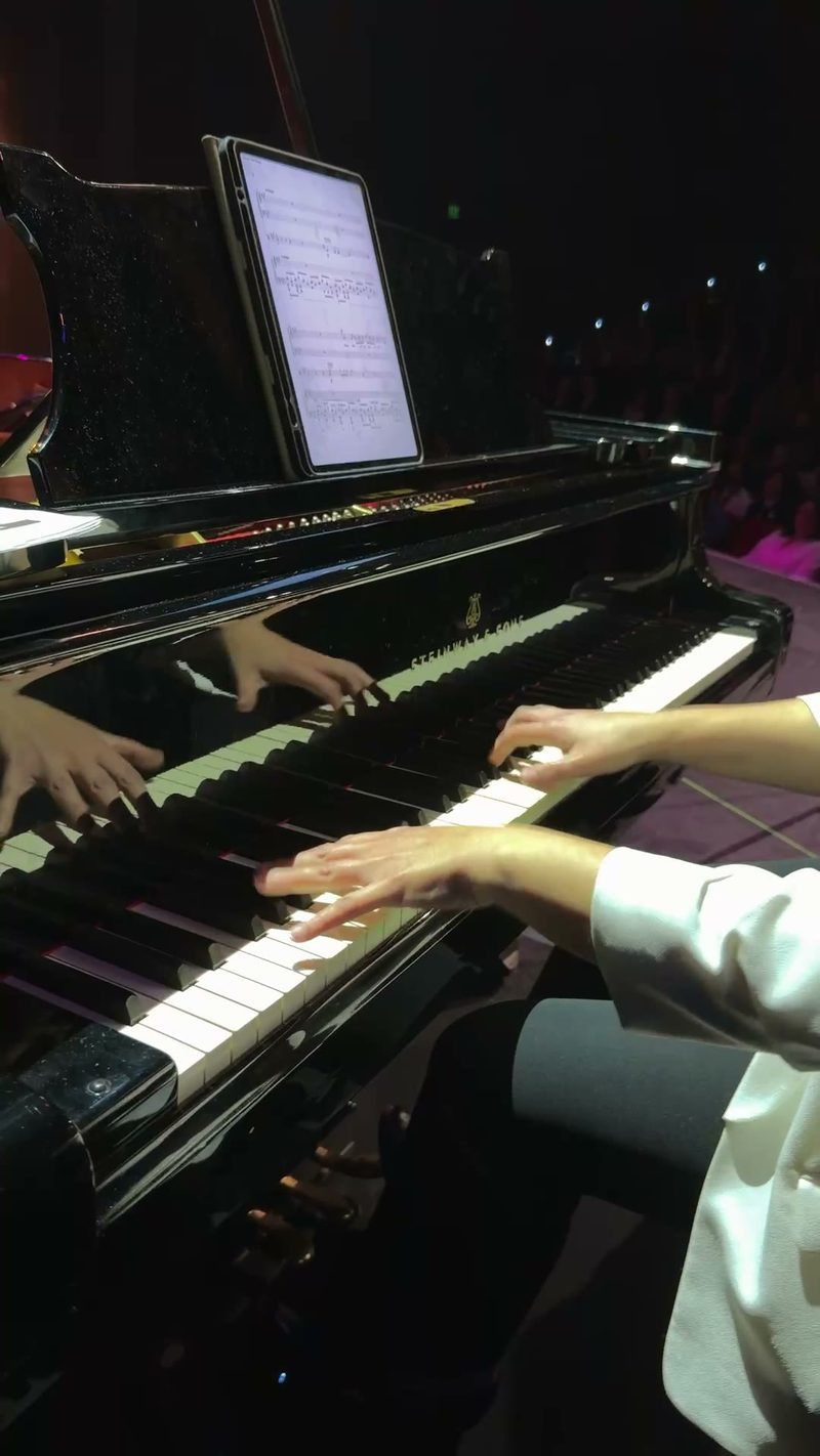 A pianist performing live on stage with sheet music visible on a tablet.