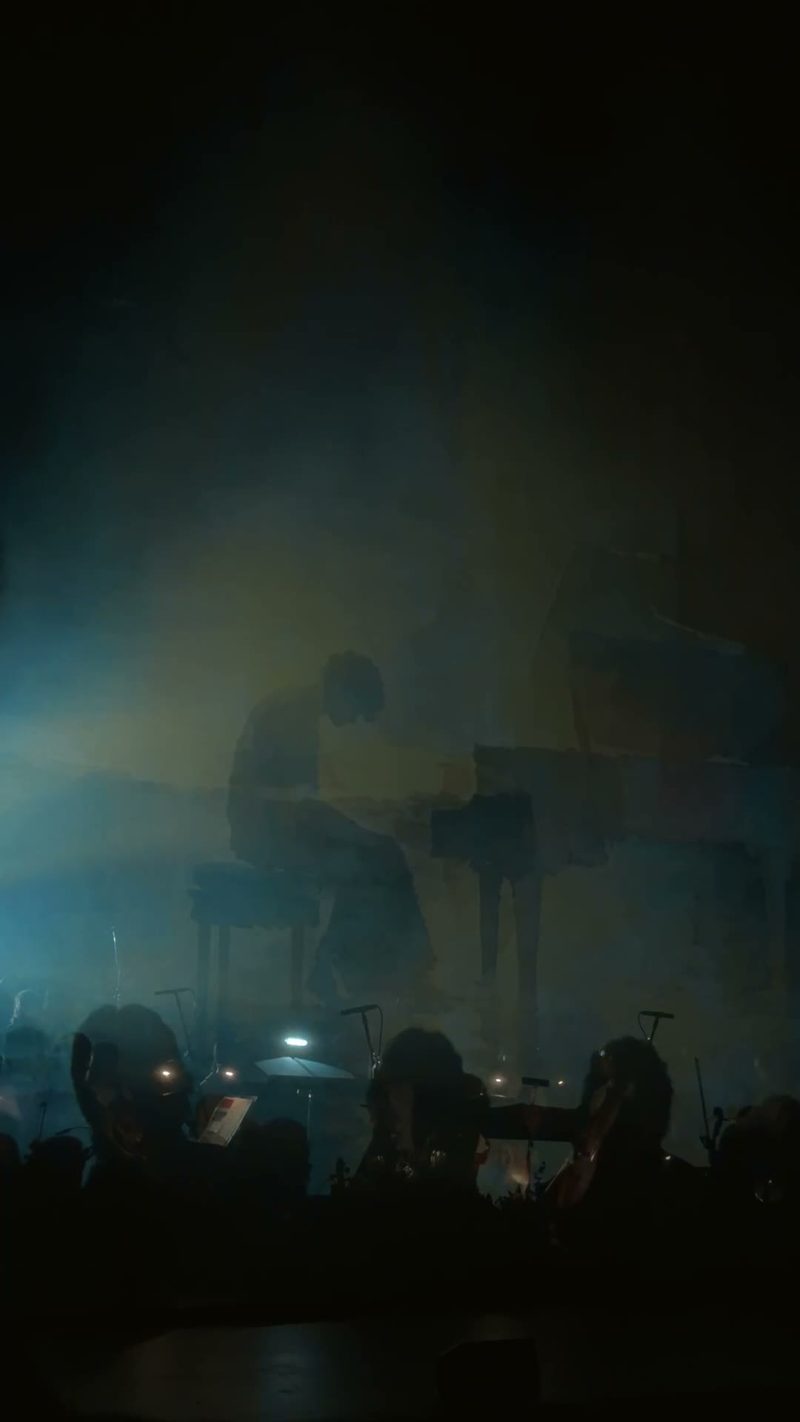 A pianist silhouetted in a misty atmosphere during a performance with an orchestra.