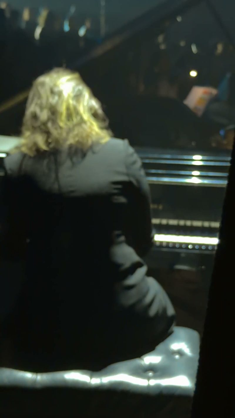 A performer playing a grand piano in a dimly lit setting.