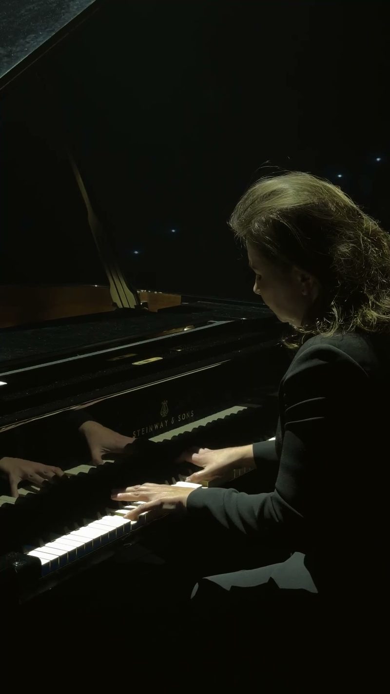 A pianist performing on a grand piano in a dimly lit setting.