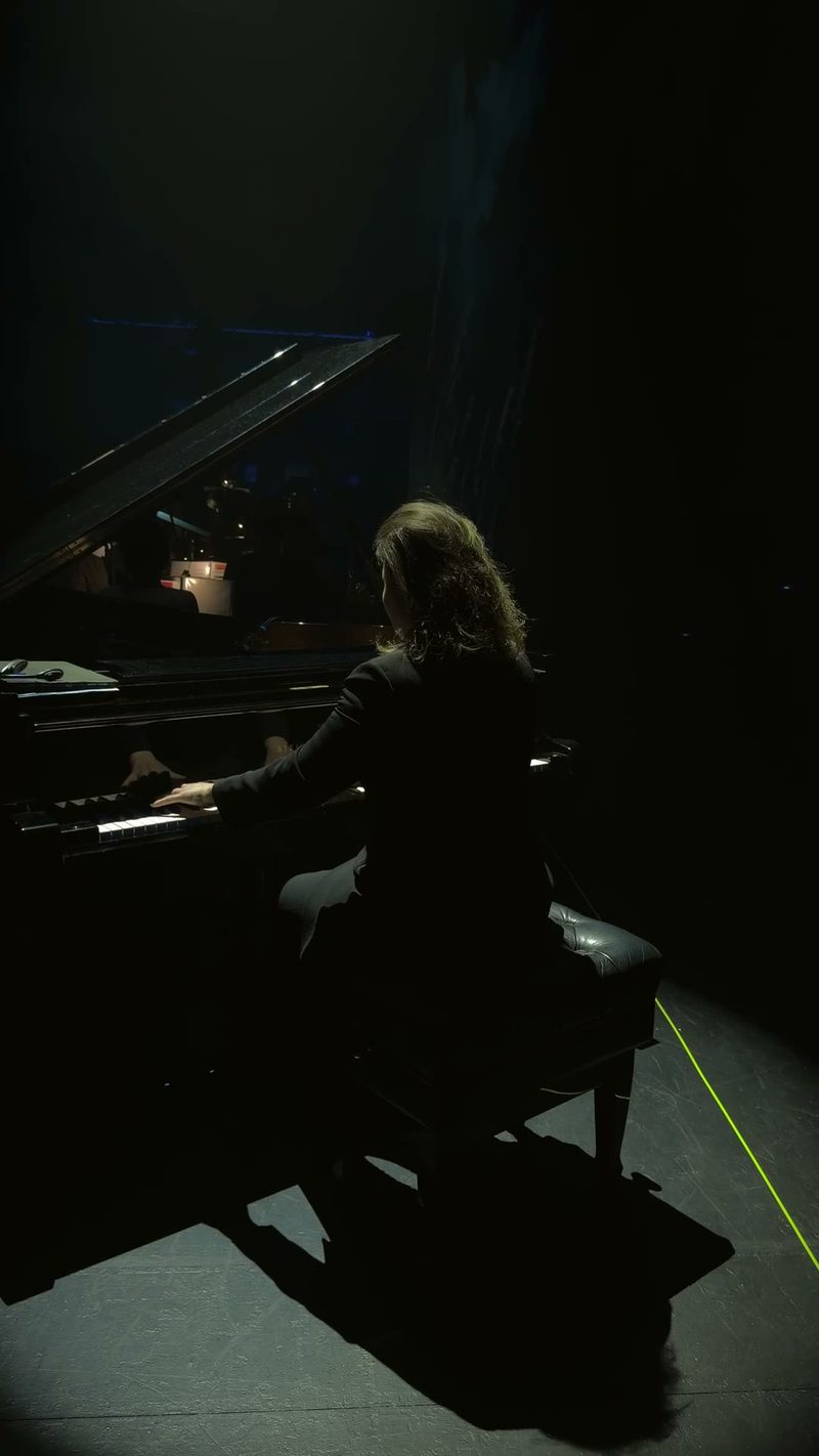 A performer playing the piano under dramatic stage lighting.