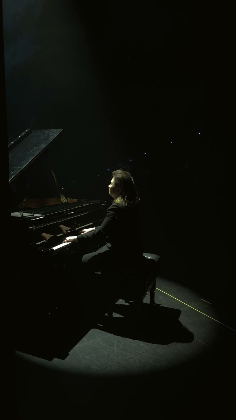 A pianist performing on stage with an elegant backdrop of darkness.