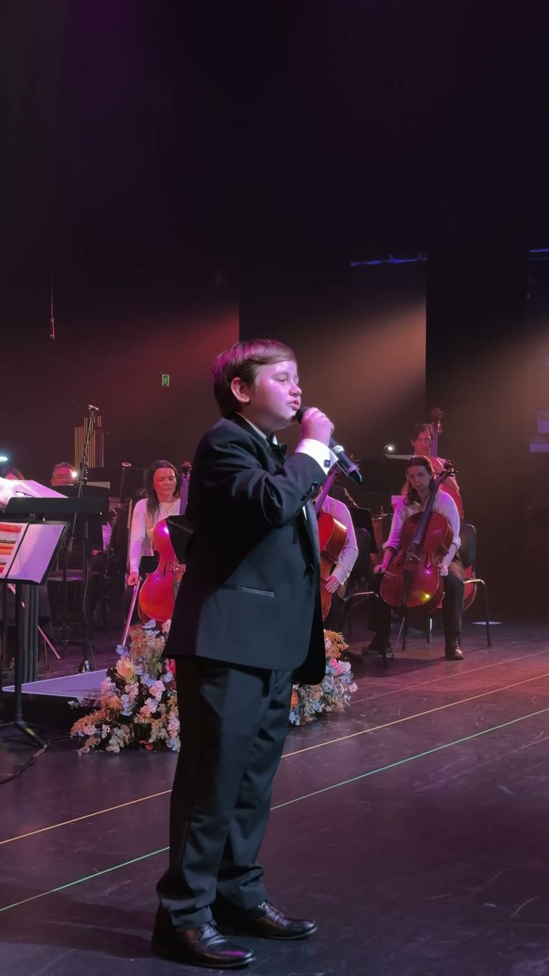 A young boy performs solo in front of a symphony orchestra.