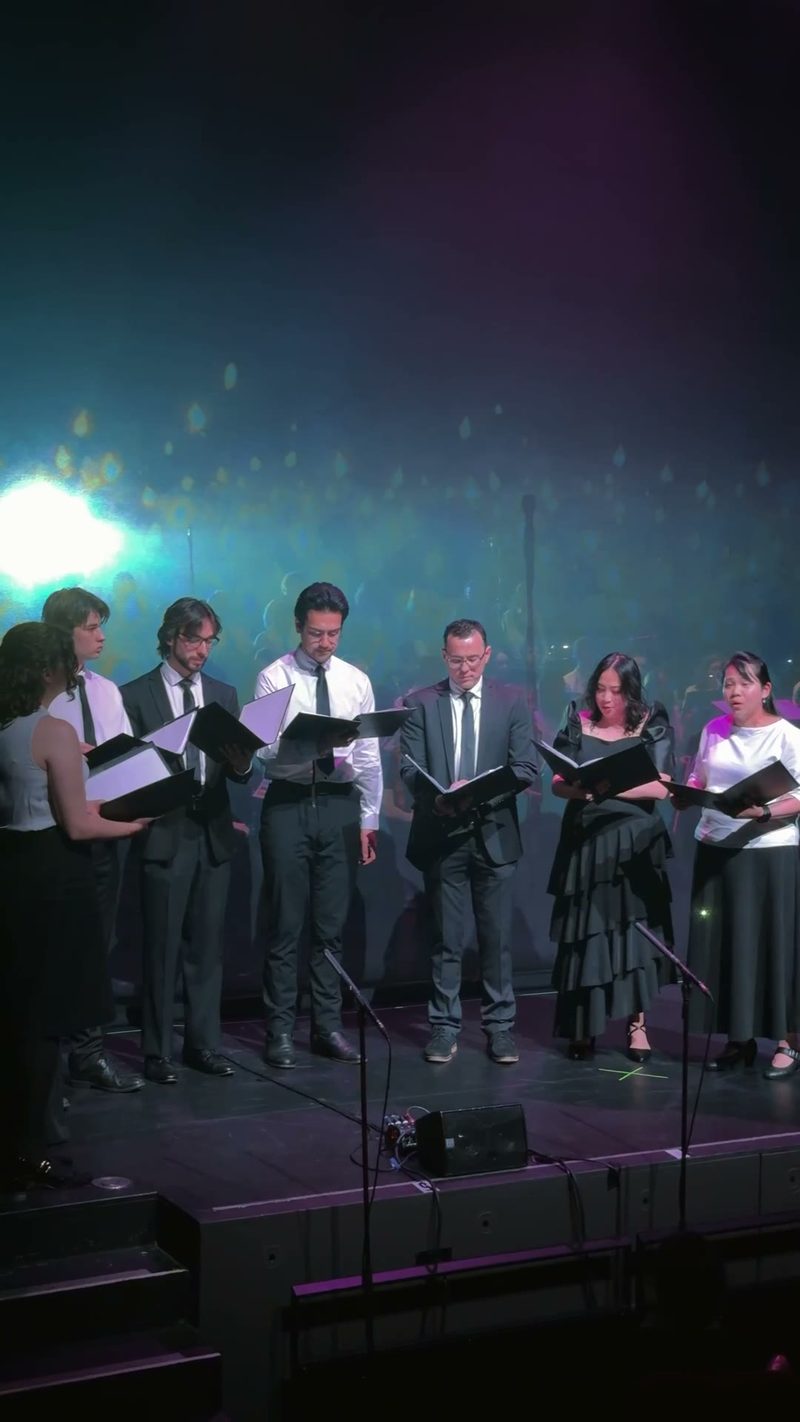 A choral group performing on stage with music sheets in hand.