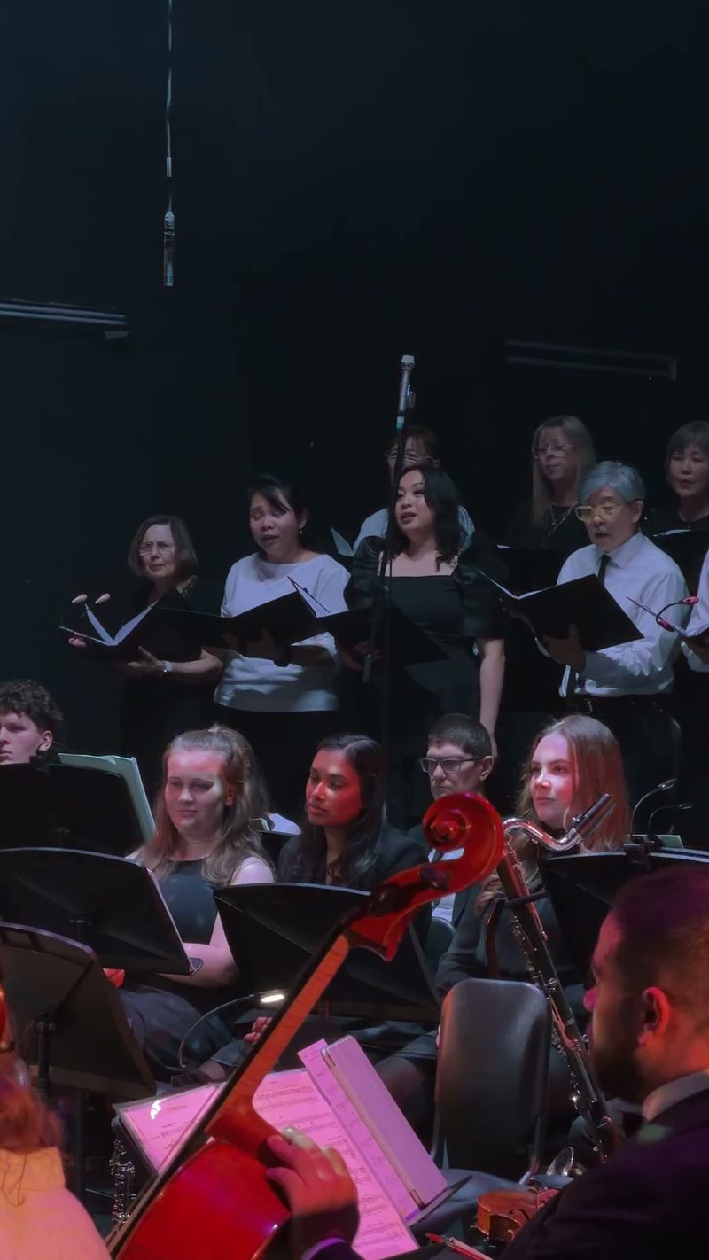 A choir performing on stage with an orchestra during a concert.