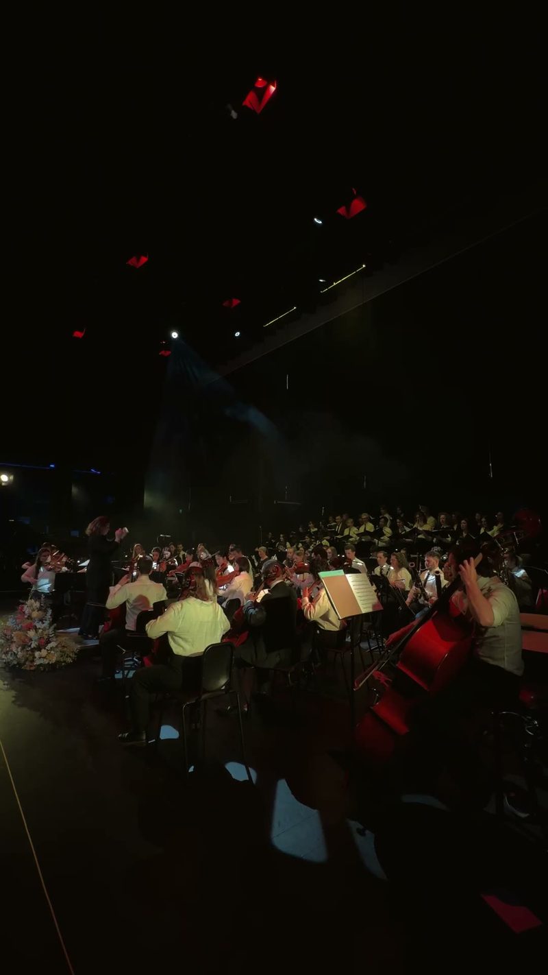 An orchestra performs under dramatic lighting on stage.