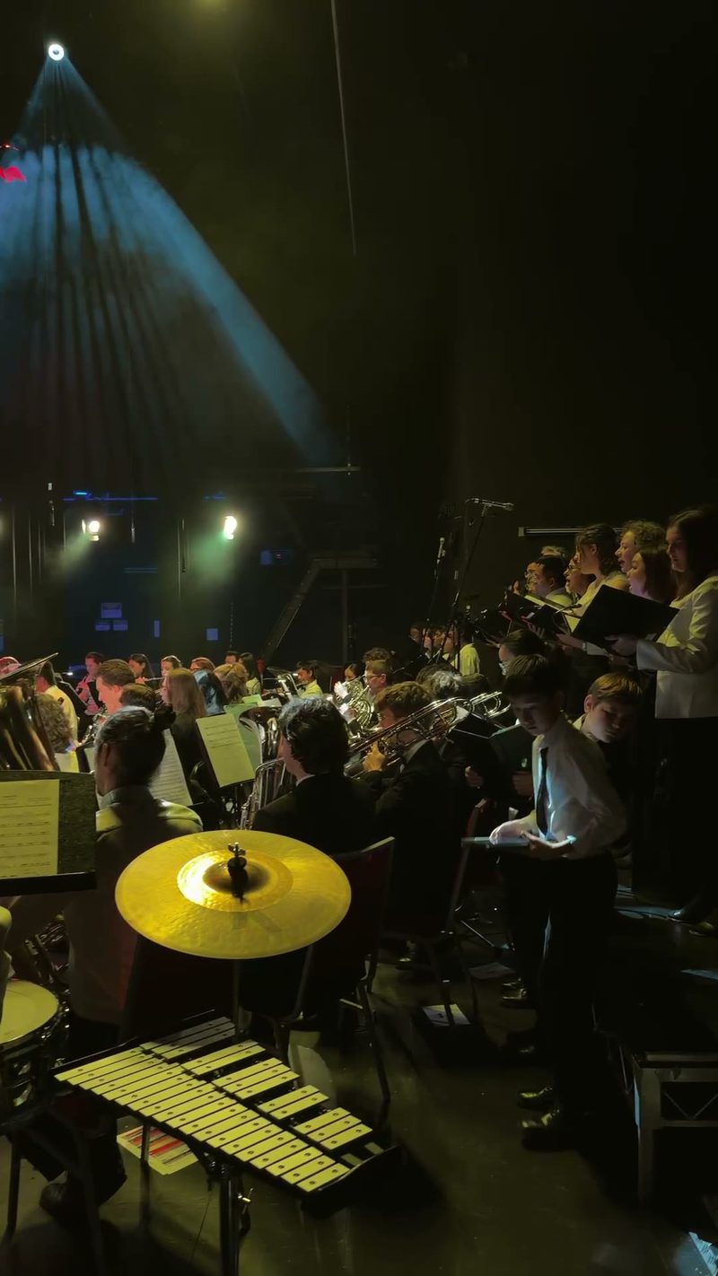 A symphony orchestra and choir perform on stage under dramatic lighting.