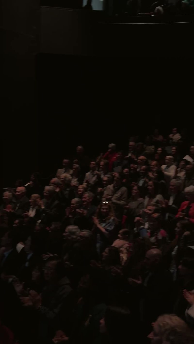 A large audience clapping in a darkened venue.