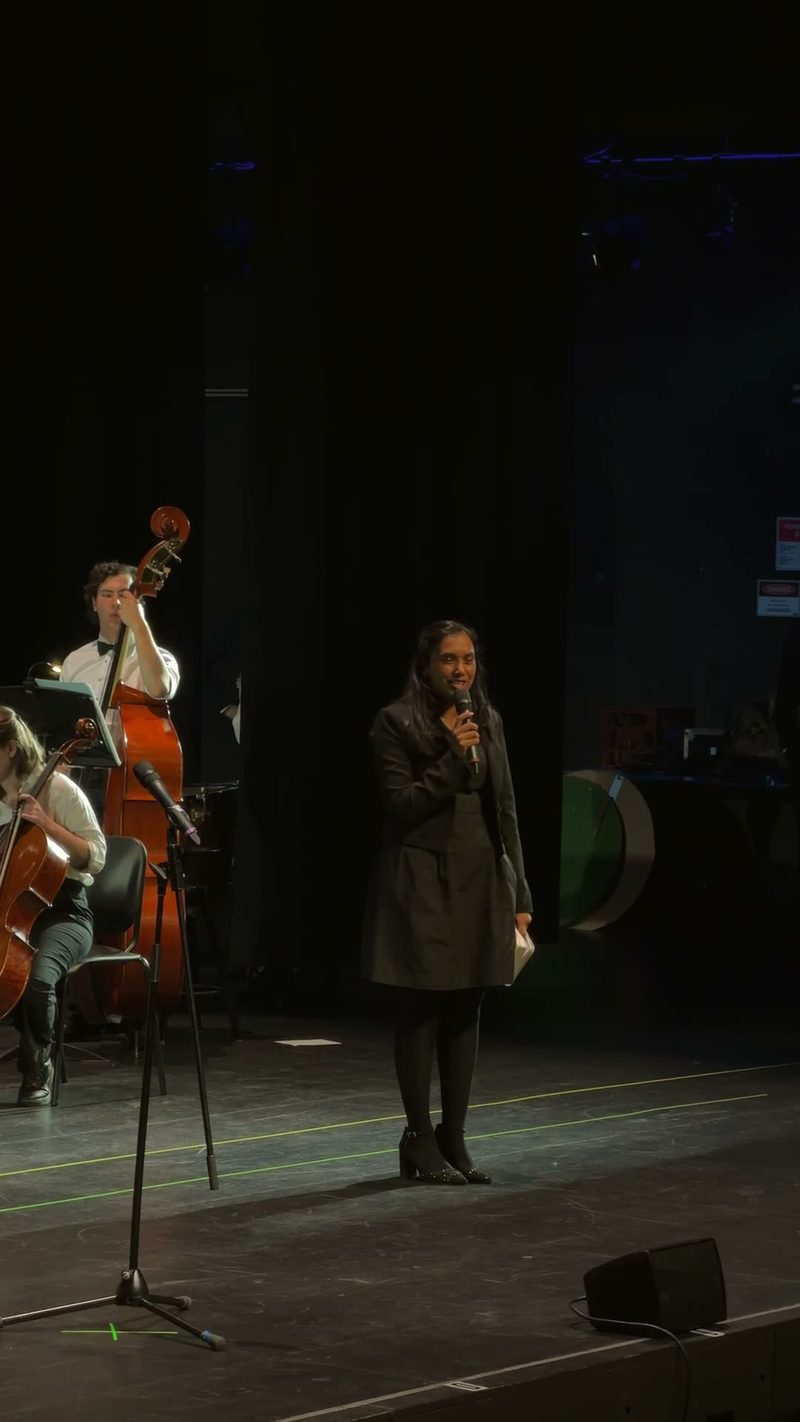 A speaker addresses the audience while musicians prepare in the background.