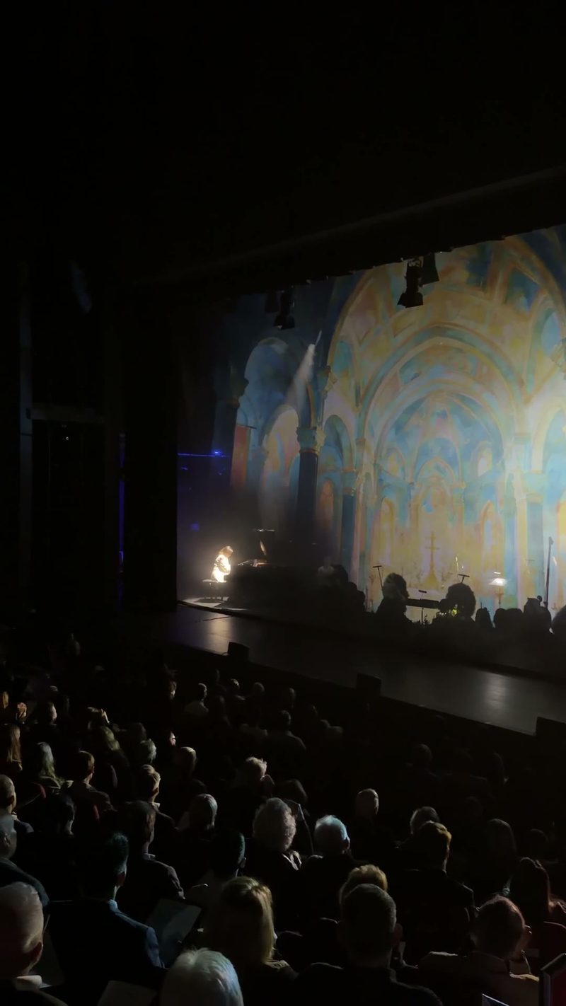 A performer plays piano in a beautifully lit venue with an ornate backdrop.