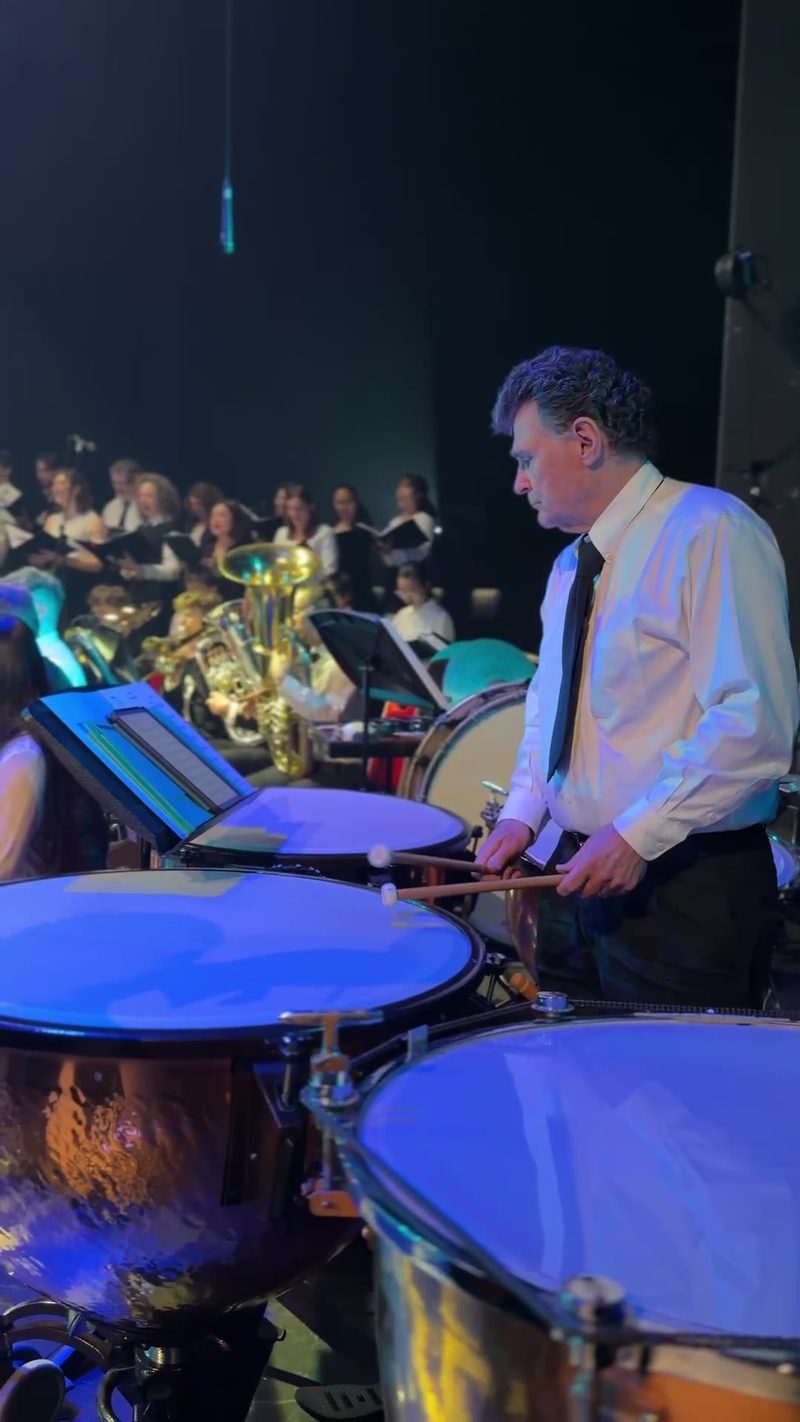 A percussionist prepares to play during a concert with a choir in the background.