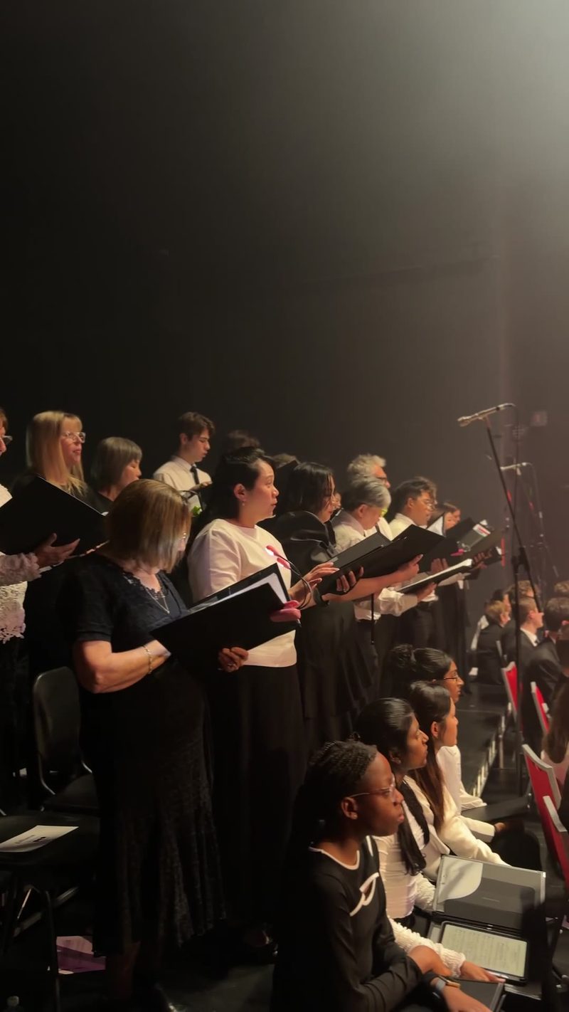 A diverse choir performing on stage with sheet music in hand.
