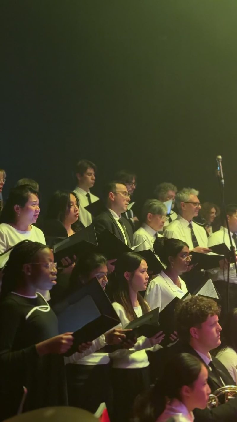 A diverse choir performing on stage with sheet music in hand.