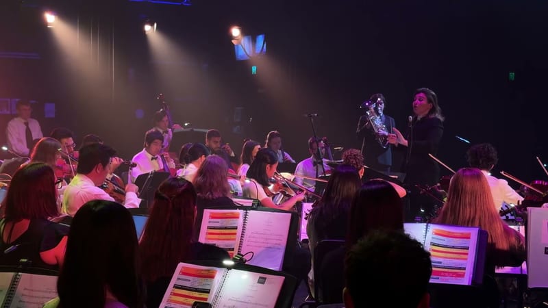A symphony orchestra performing on stage with a conductor and various musicians visible.