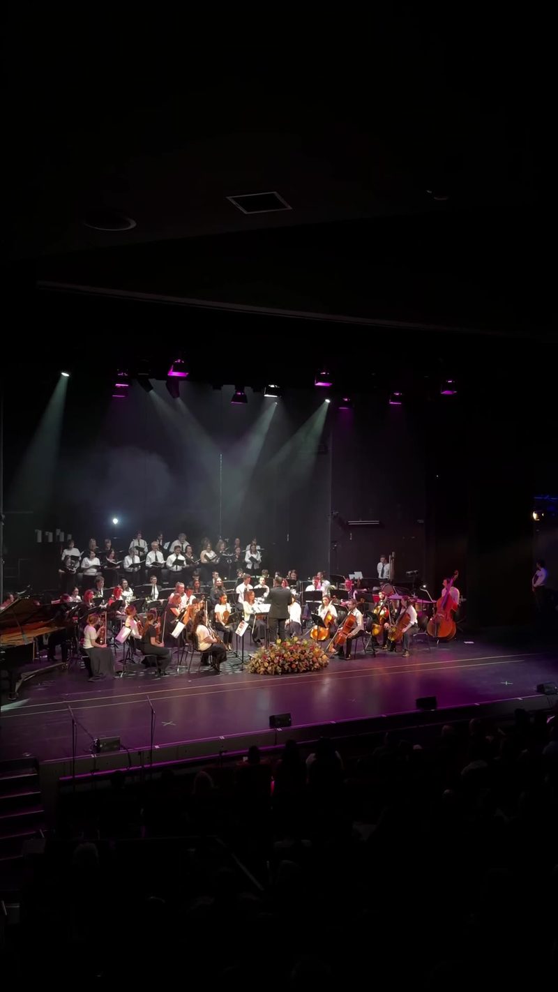 A full orchestra and choir performing on stage under dramatic lighting.