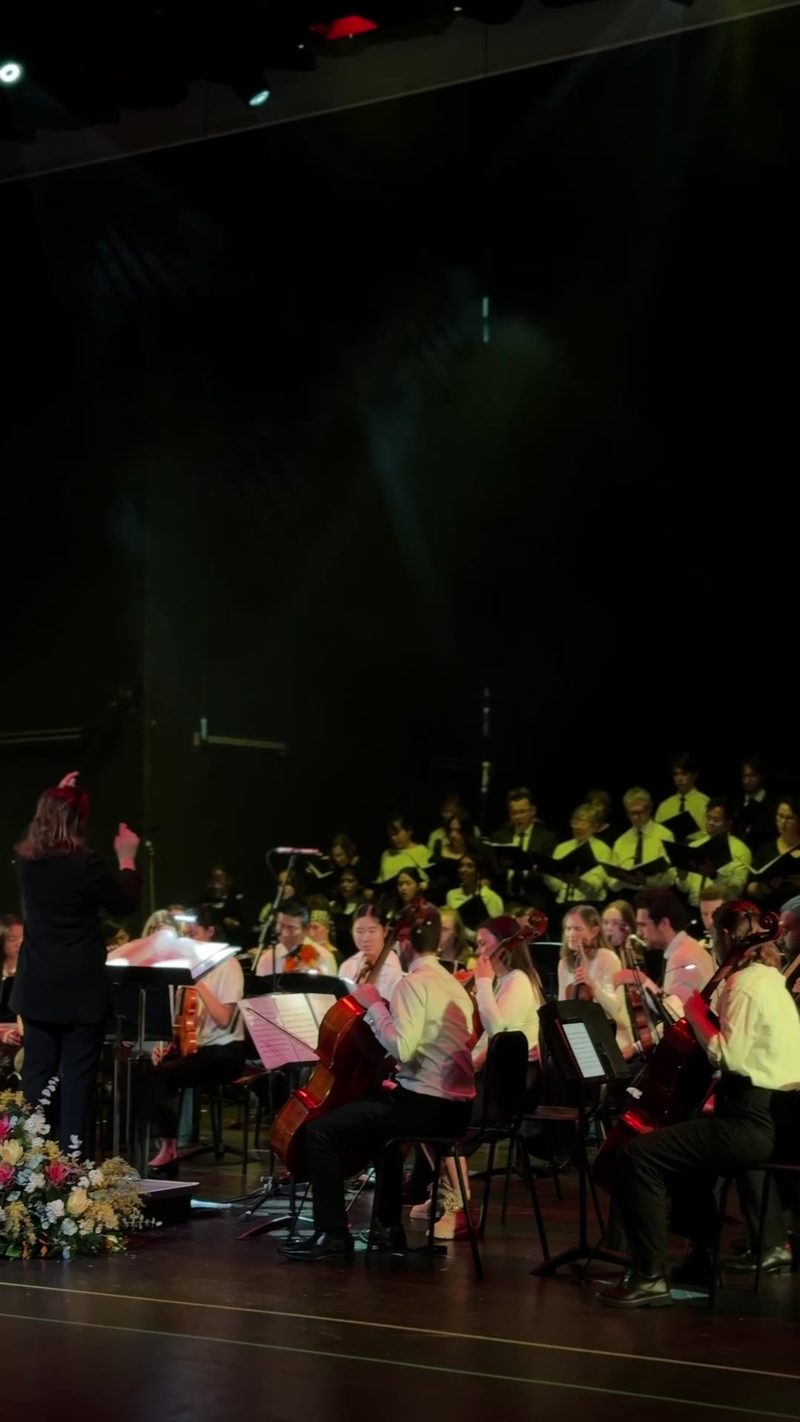 A conductor leading a symphony orchestra performance with a choir in the background.