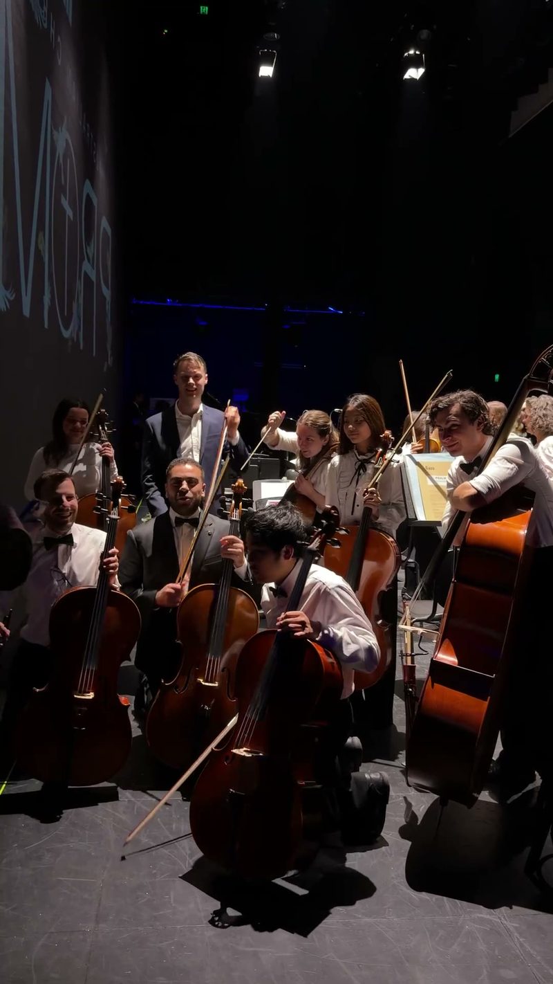 A group of musicians posing together with their cellos backstage.