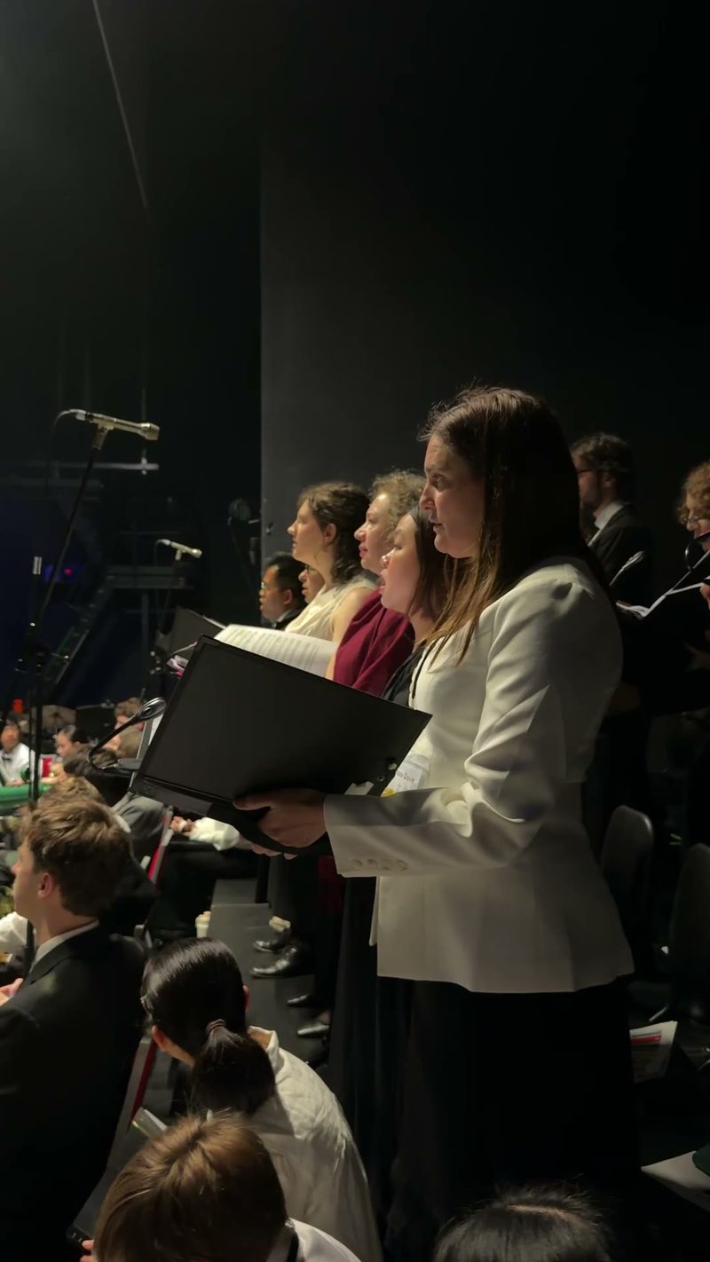 A group of choir members performing on stage with sheet music in hand.