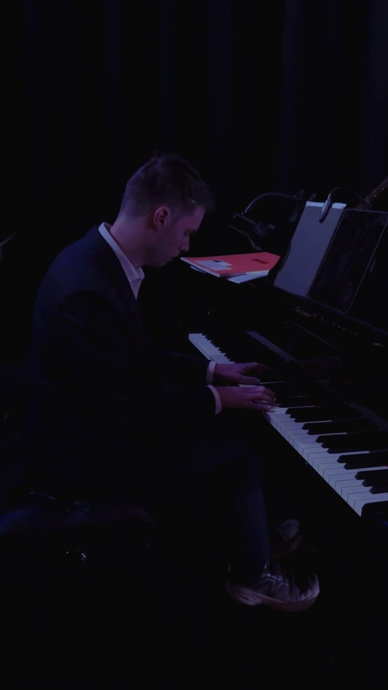 A pianist performing at a concert with a dark backdrop.