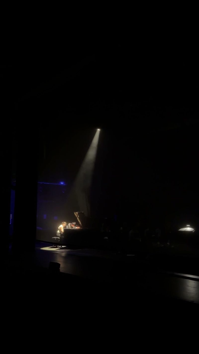 A performer playing the piano under a spotlight during a concert.