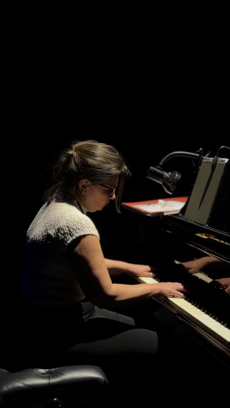 A performer playing piano on stage in a dimly lit setting.