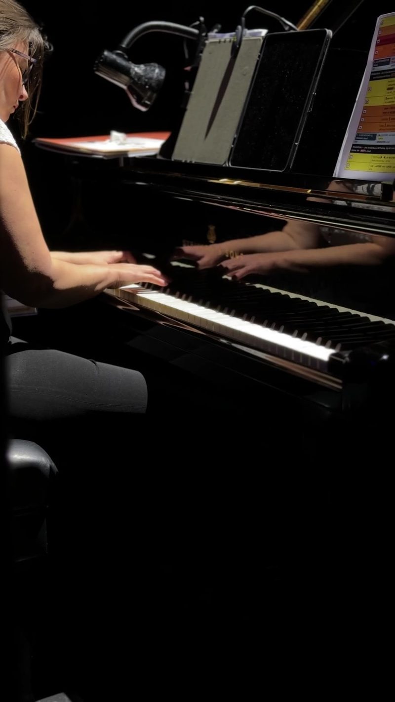 A pianist performing at a grand piano, illuminated by a focused lamp.