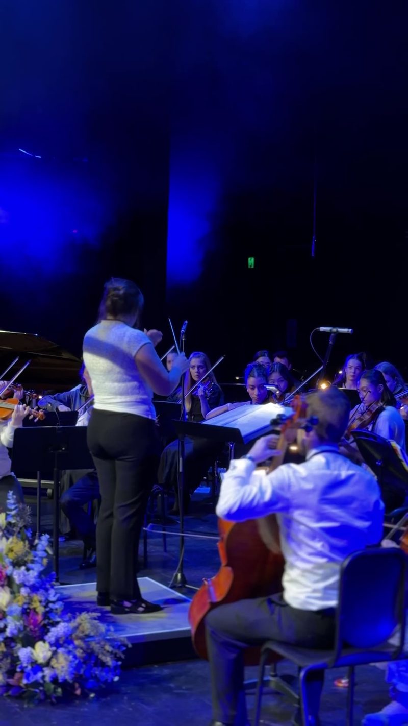 A symphony orchestra performing on stage with a conductor leading the musicians.