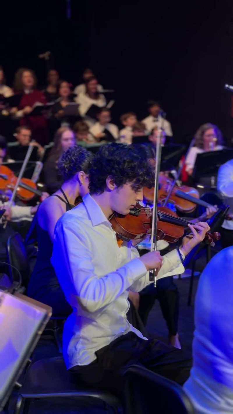 A young violinist performing in an orchestra setting.