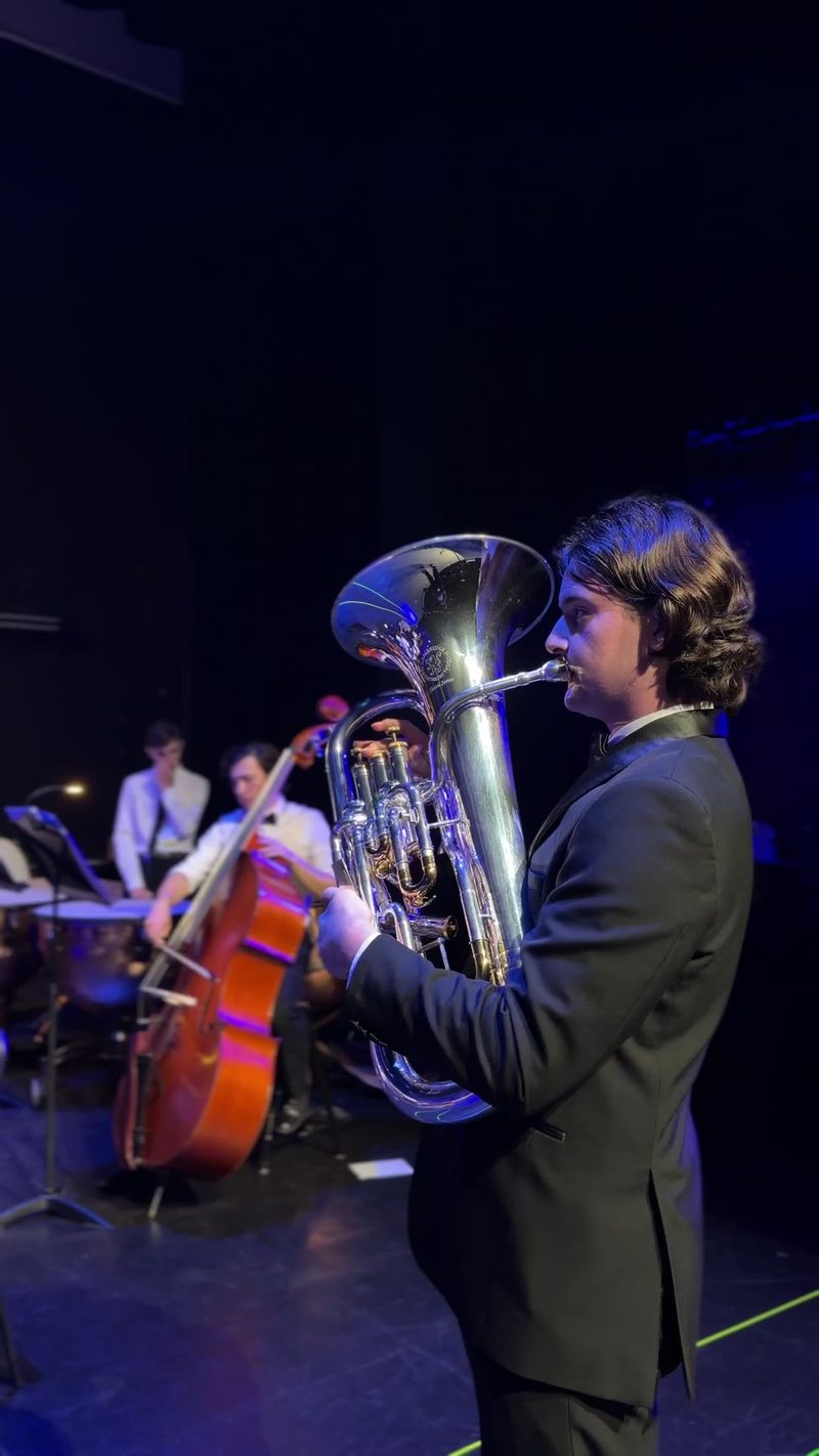 A tuba player performs on stage in front of an ensemble.
