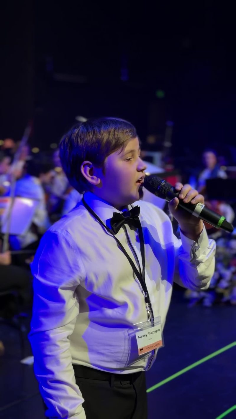 A young soloist sings into a microphone during a performance.