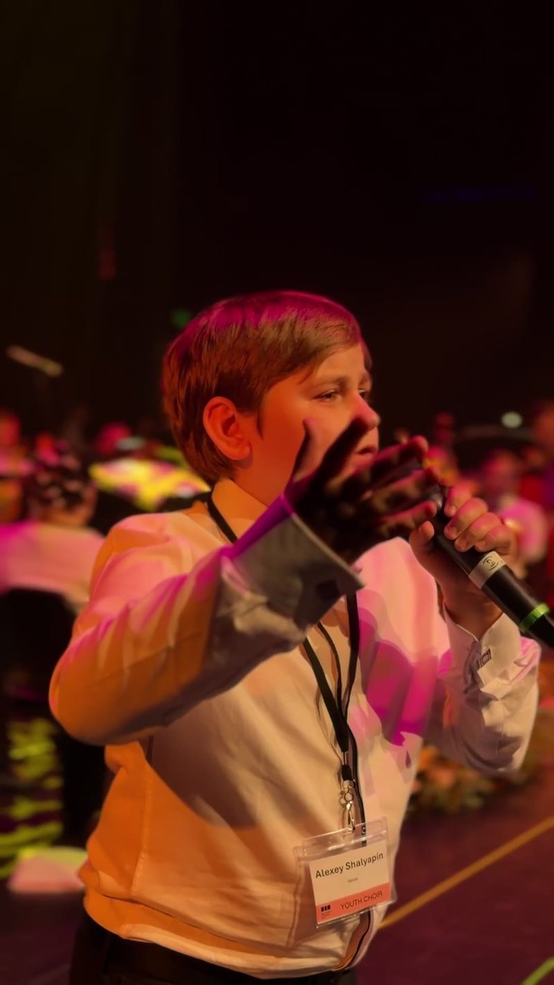 A young soloist passionately sings on stage with a microphone during a performance.
