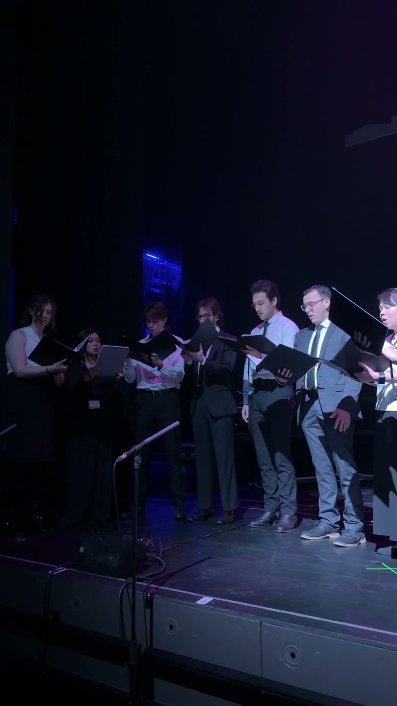 A choral group performing on stage with illuminated backdrops.