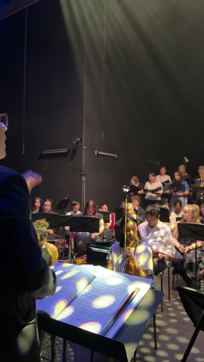 A conductor leads a symphony orchestra and choir during a rehearsal.