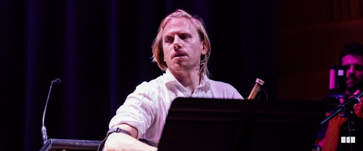 A male pianist in a white shirt performs intently at a grand piano on a concert stage.